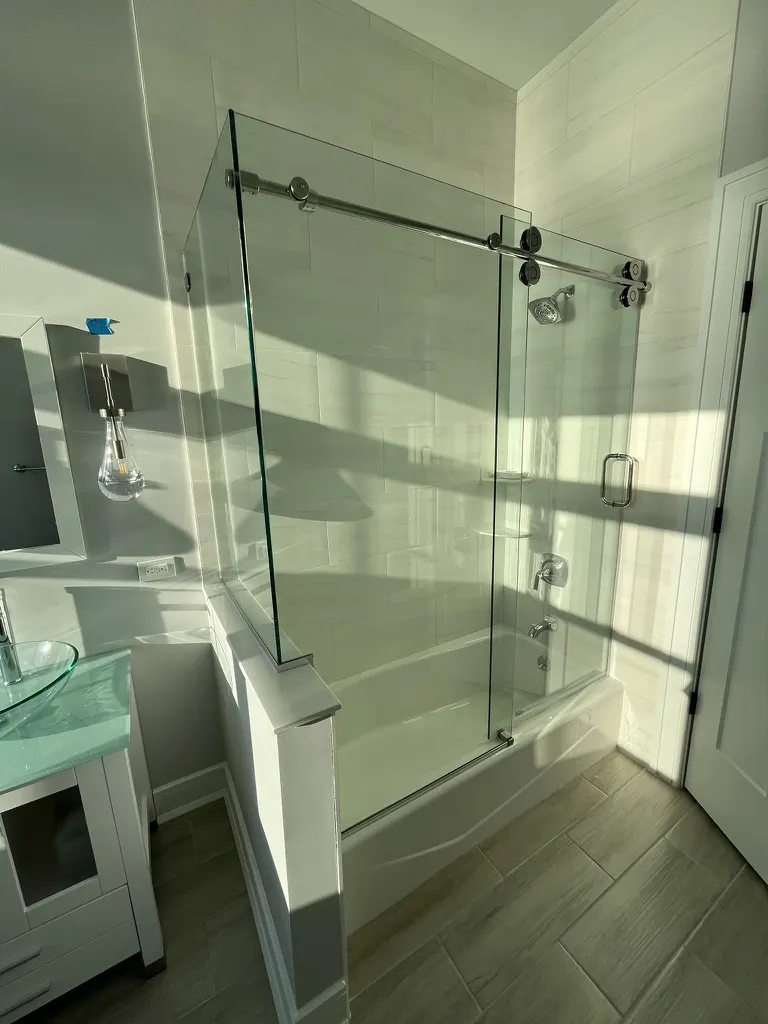 Sliding barn-hardware tub enclosure with a green glass vanity top and a glass vessel basin in the foreground.