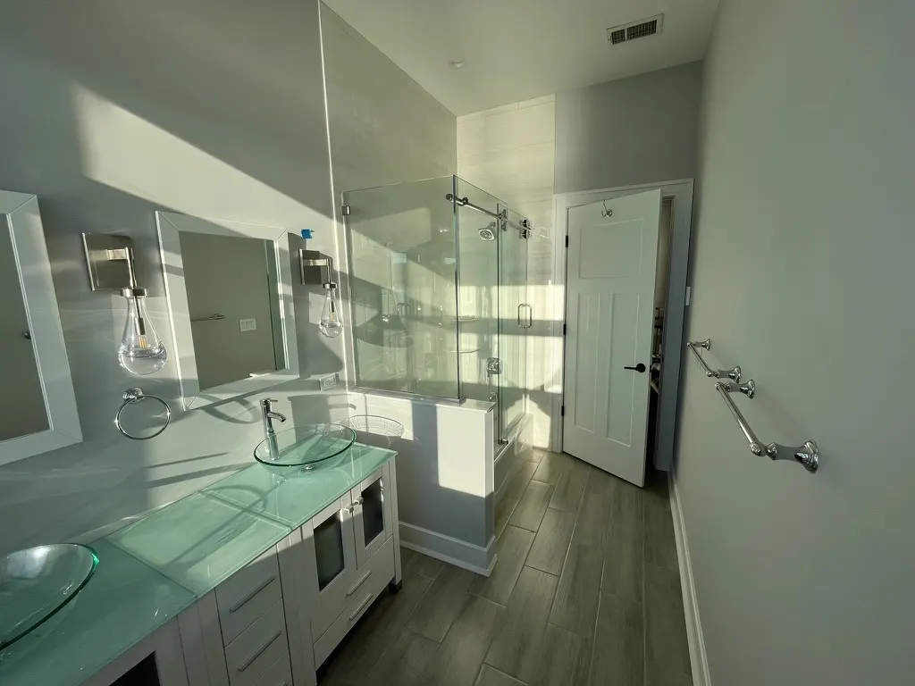 Bathroom with green glass vessel basins on a glass countertop, and a neo-angle glass shower enclosure behind.