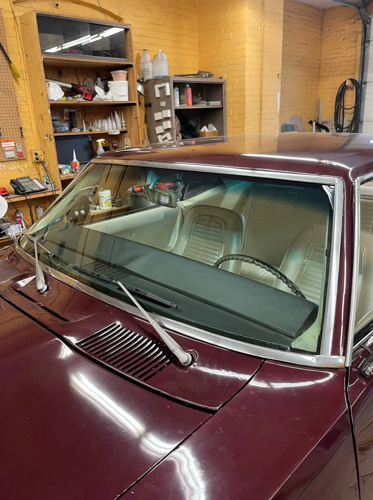 Classic maroon coupe in the Mesko Glass shop bay with a freshly set windshield and polished chrome trim