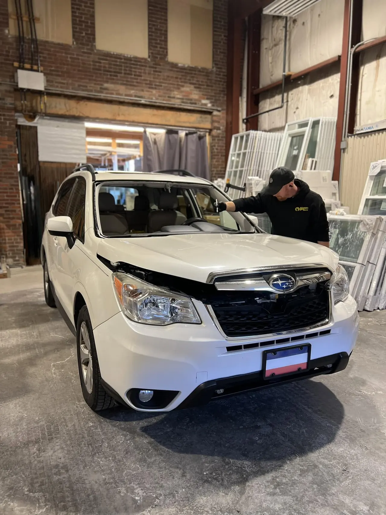 Technician in a company cap setting a new windshield into a white SUV inside the glass shop