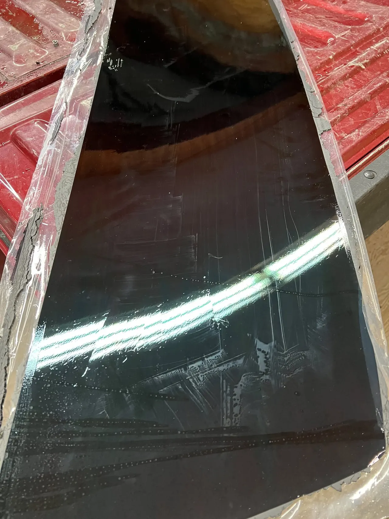 Tinted vehicle back glass wrapped in protective plastic resting in a red pickup truck bed