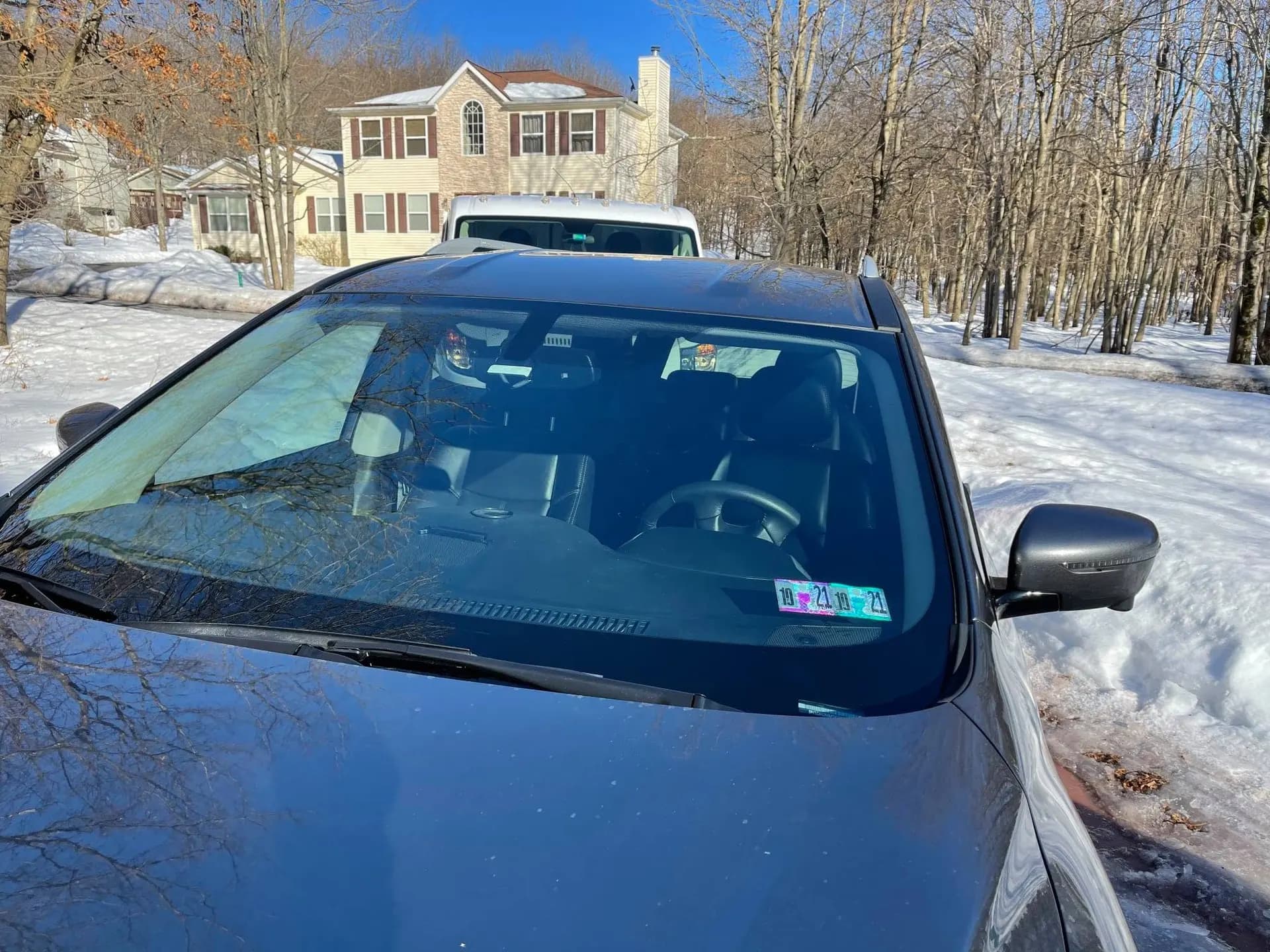 Vehicle in a snowy driveway with a freshly installed windshield and new inspection stickers.