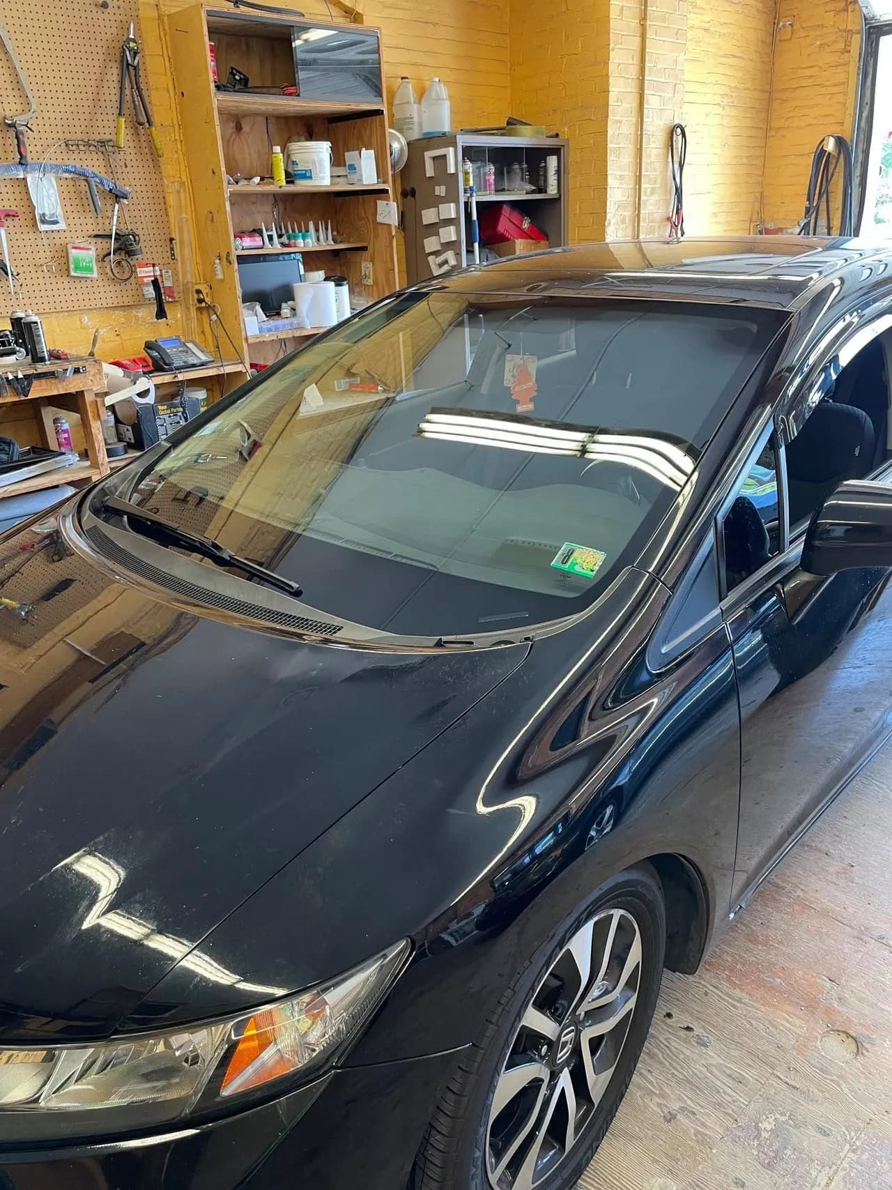 Sedan in the auto glass bay with a newly set windshield and the tool bench alongside