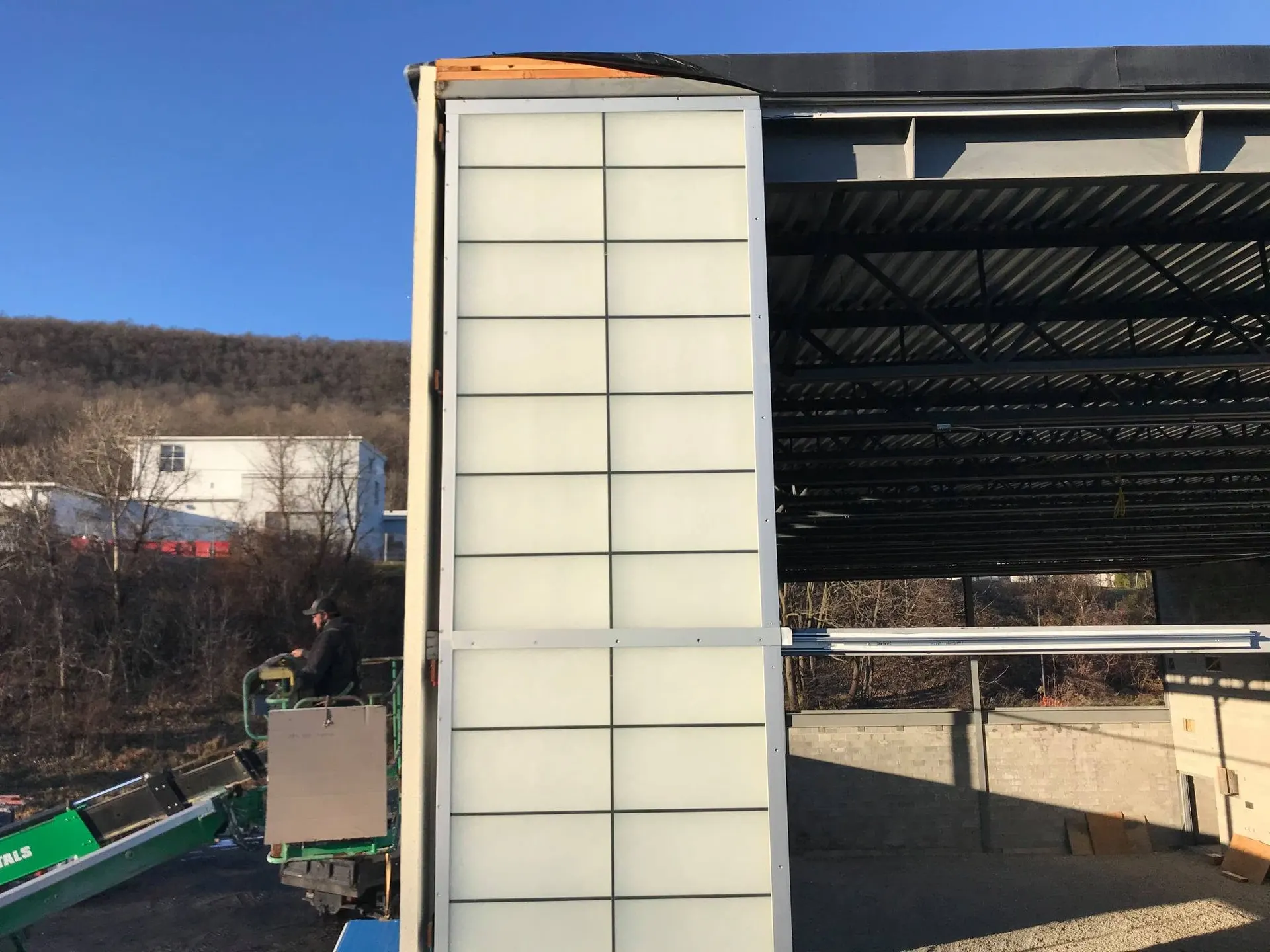 Large translucent glazing panel hoisted into a steel-framed commercial building under construction.
