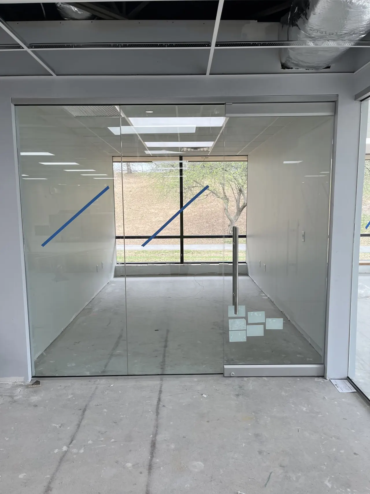 Frameless glass office partition and glass door newly set in a bare commercial space with curtain wall glazing.