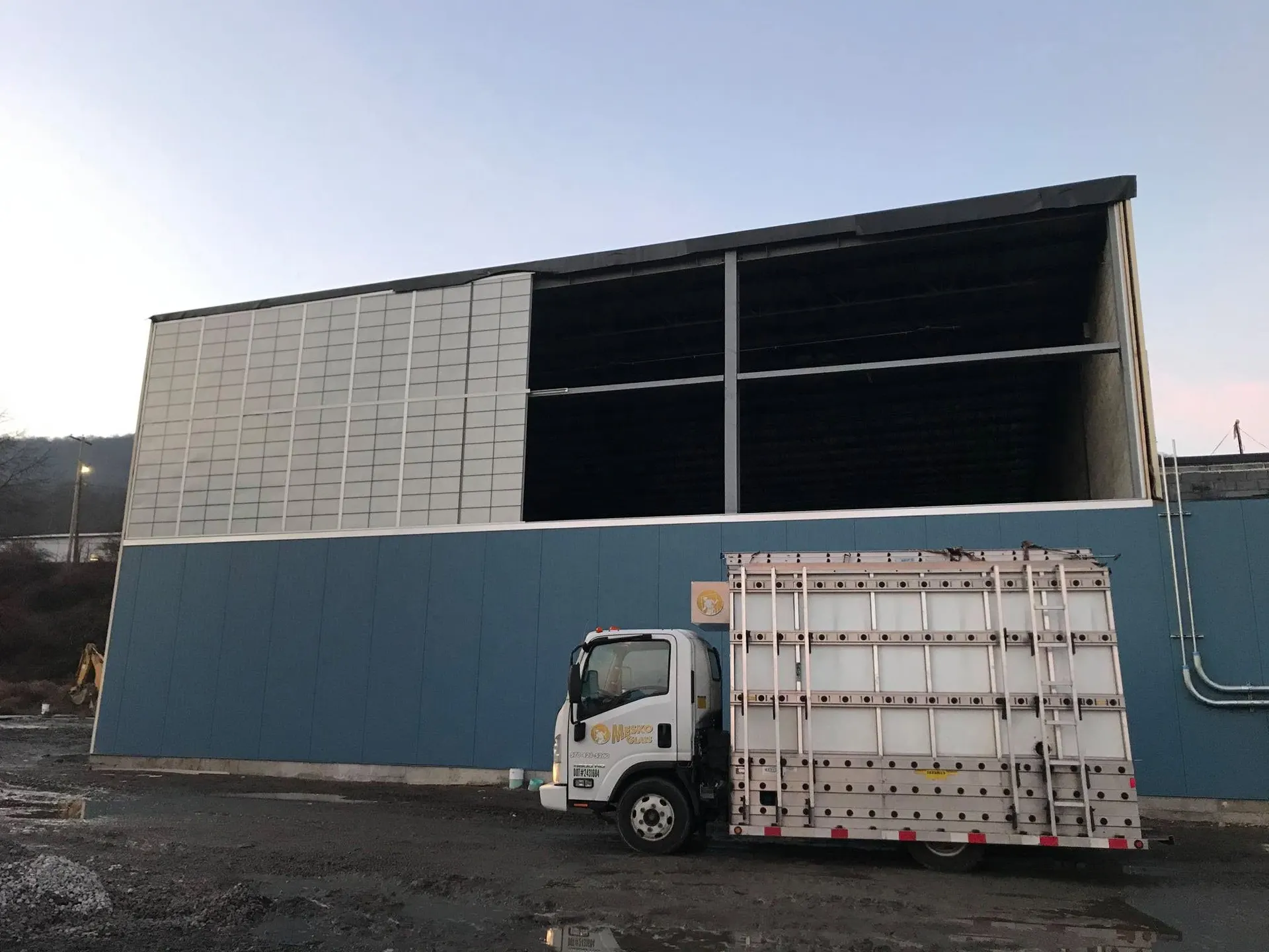 Glass rack truck parked beneath a newly glazed translucent panel wall on a commercial building at dusk.