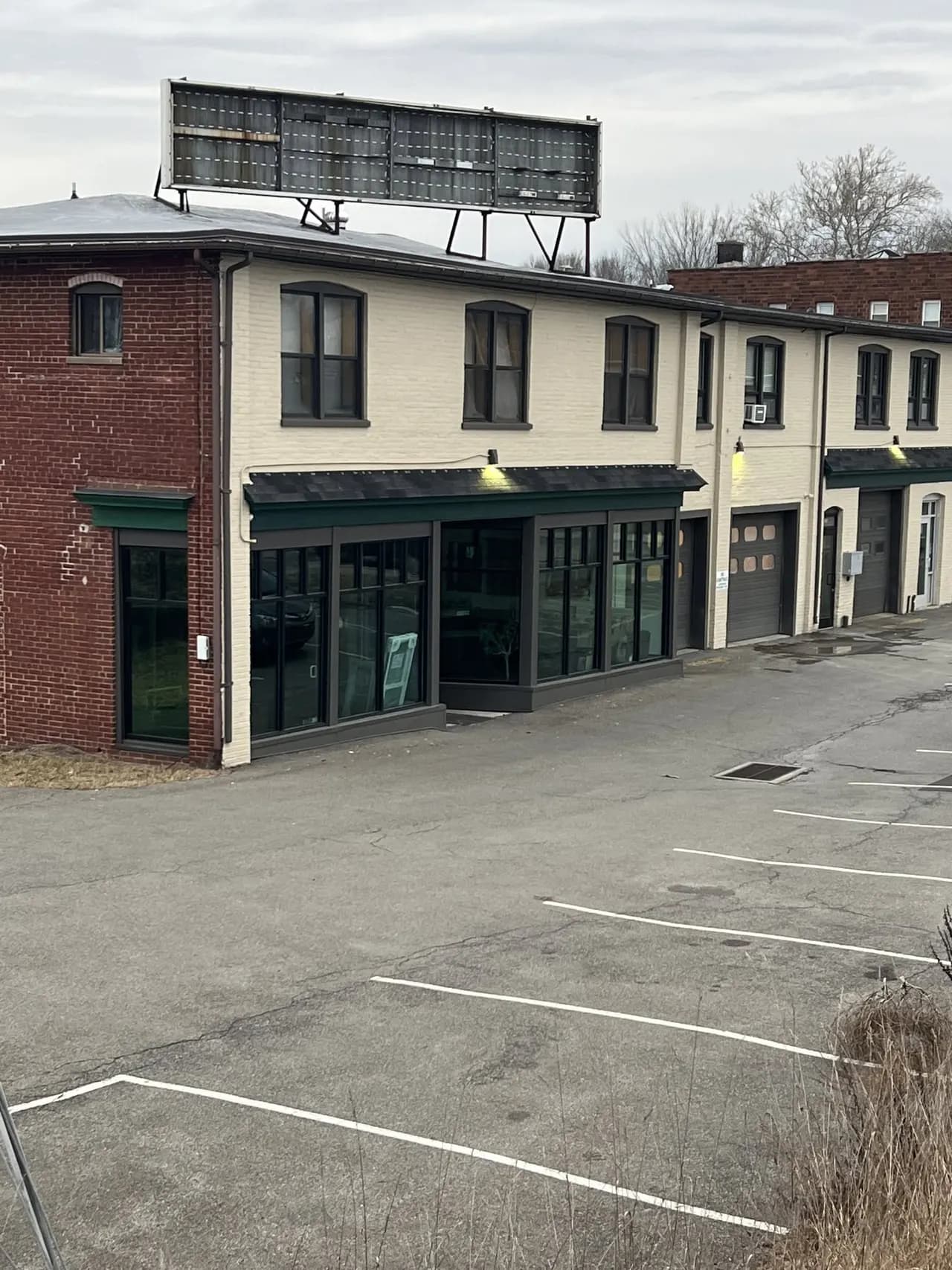 Brick and cream commercial block with a row of dark storefront glazing and a rooftop sign frame