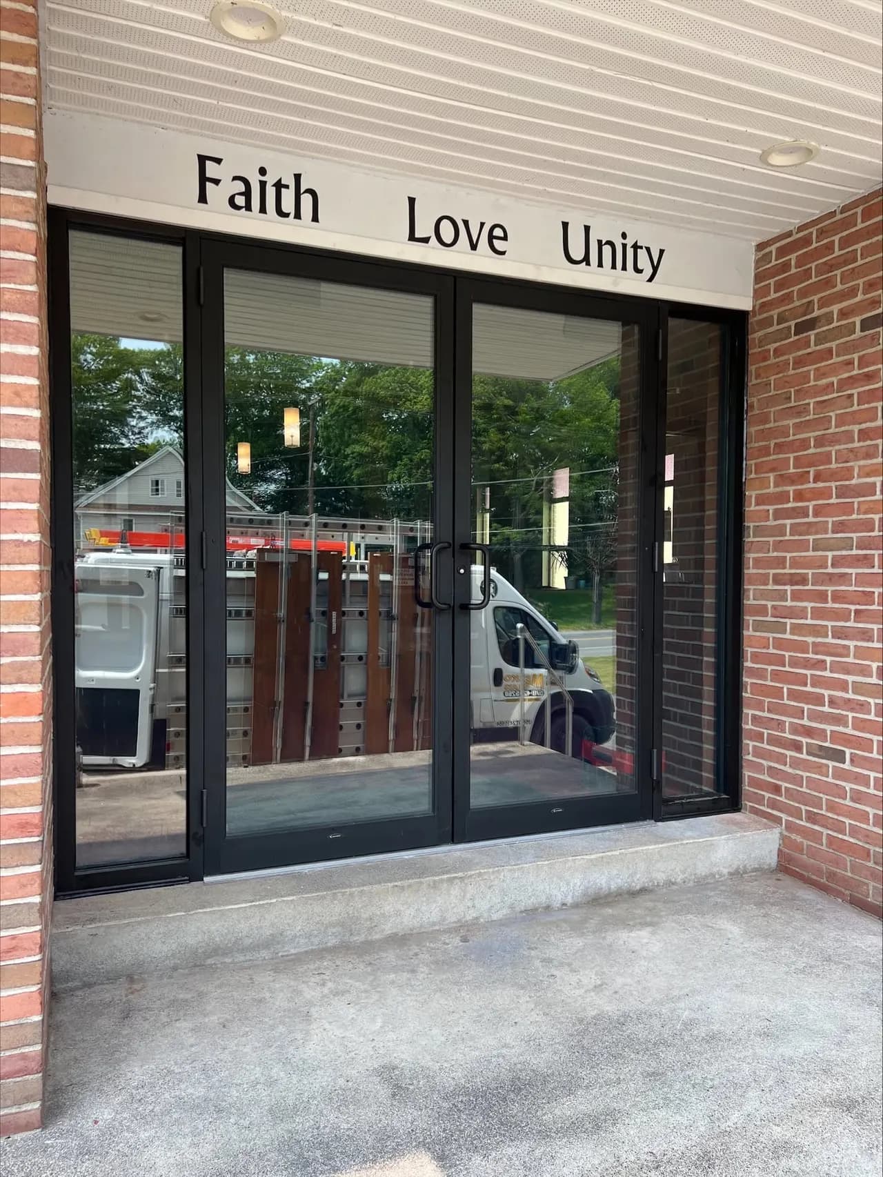 Black-framed glass double entry doors on a brick building, a company van reflected in the glass outside.