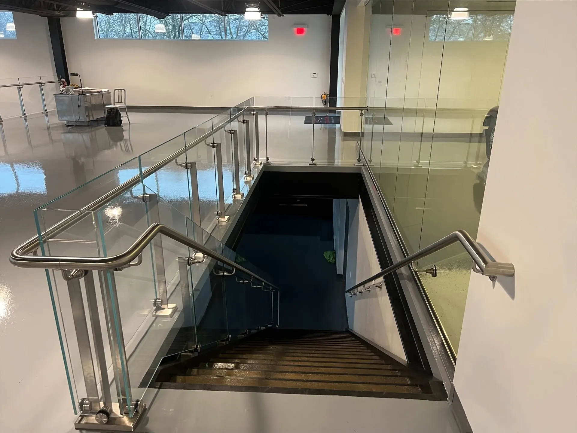 Frameless glass guardrail with a stainless handrail wrapping a stair opening in a commercial interior.