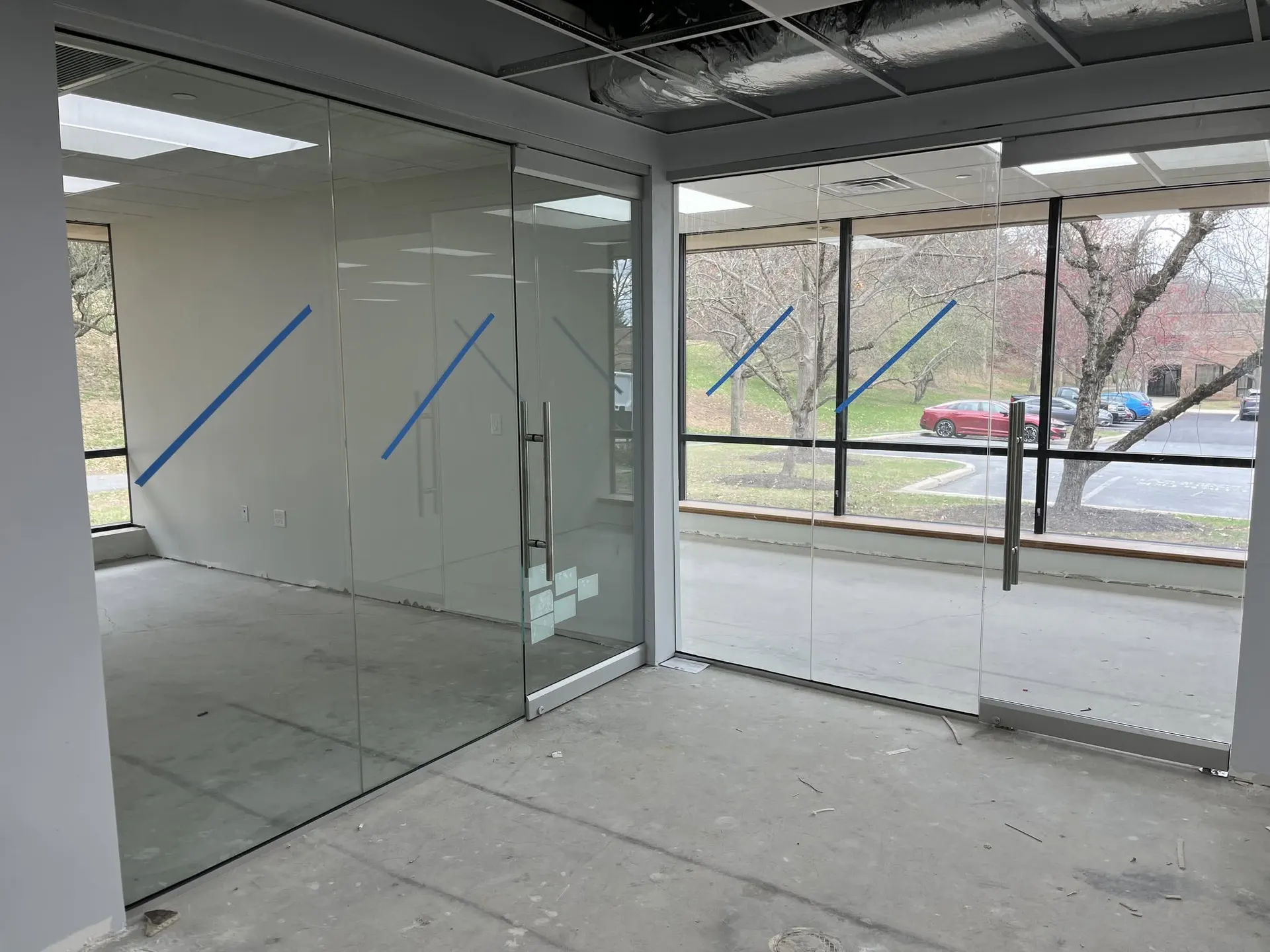 Frameless glass office partition wall with stainless pulls inside an unfinished commercial suite