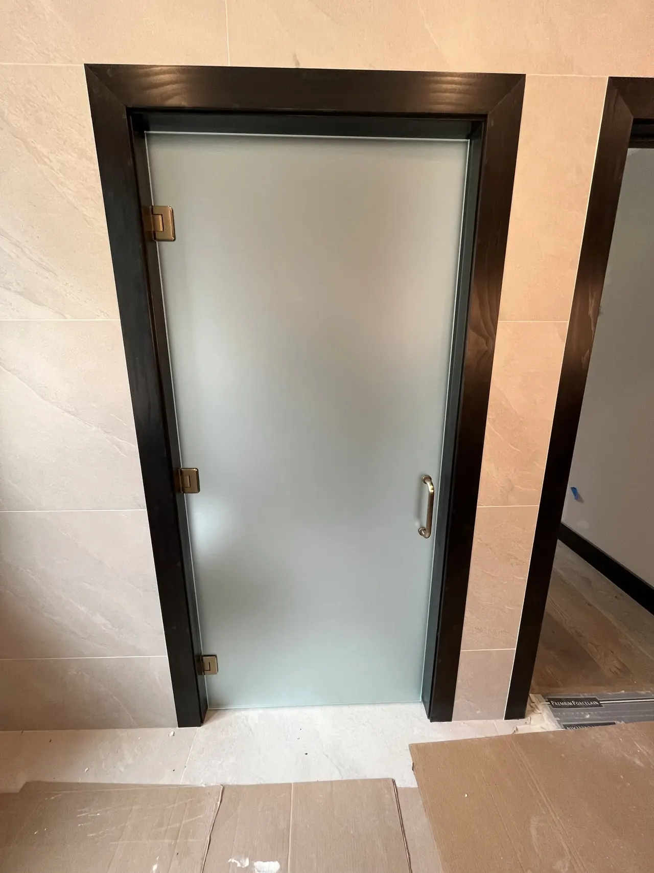 Satin frosted glass door hung in a dark wood frame in a stone-tiled interior under construction.