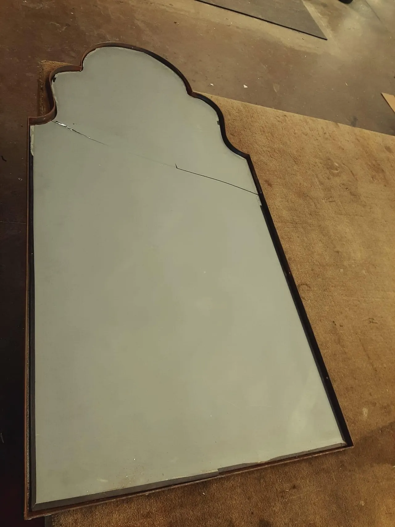Cracked antique arched mirror with a wood frame lying on a workshop table for repair