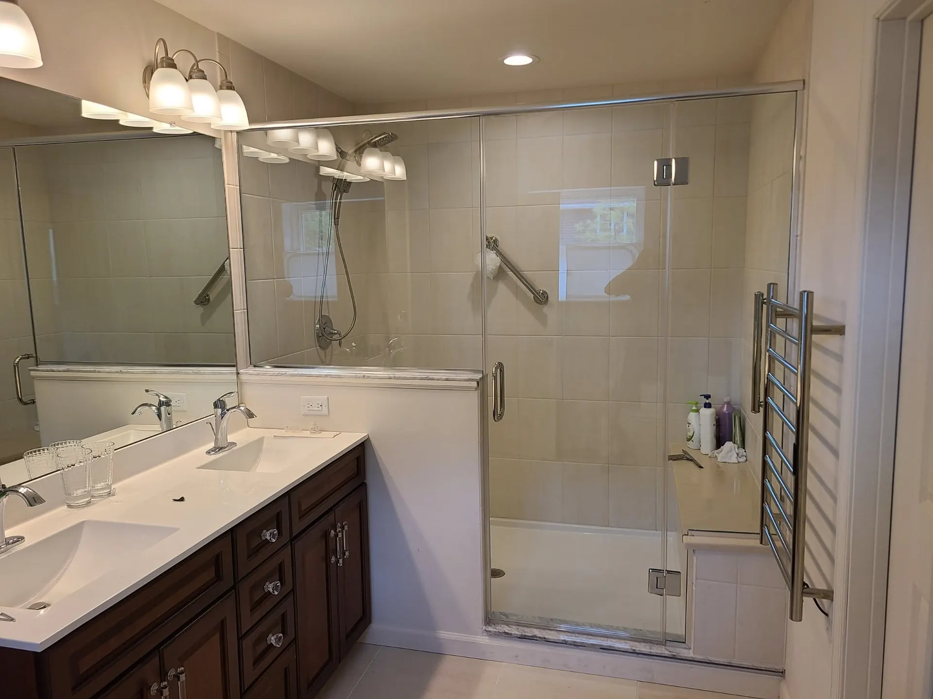 Wide frameless mirror above a double vanity beside a framed glass shower enclosure