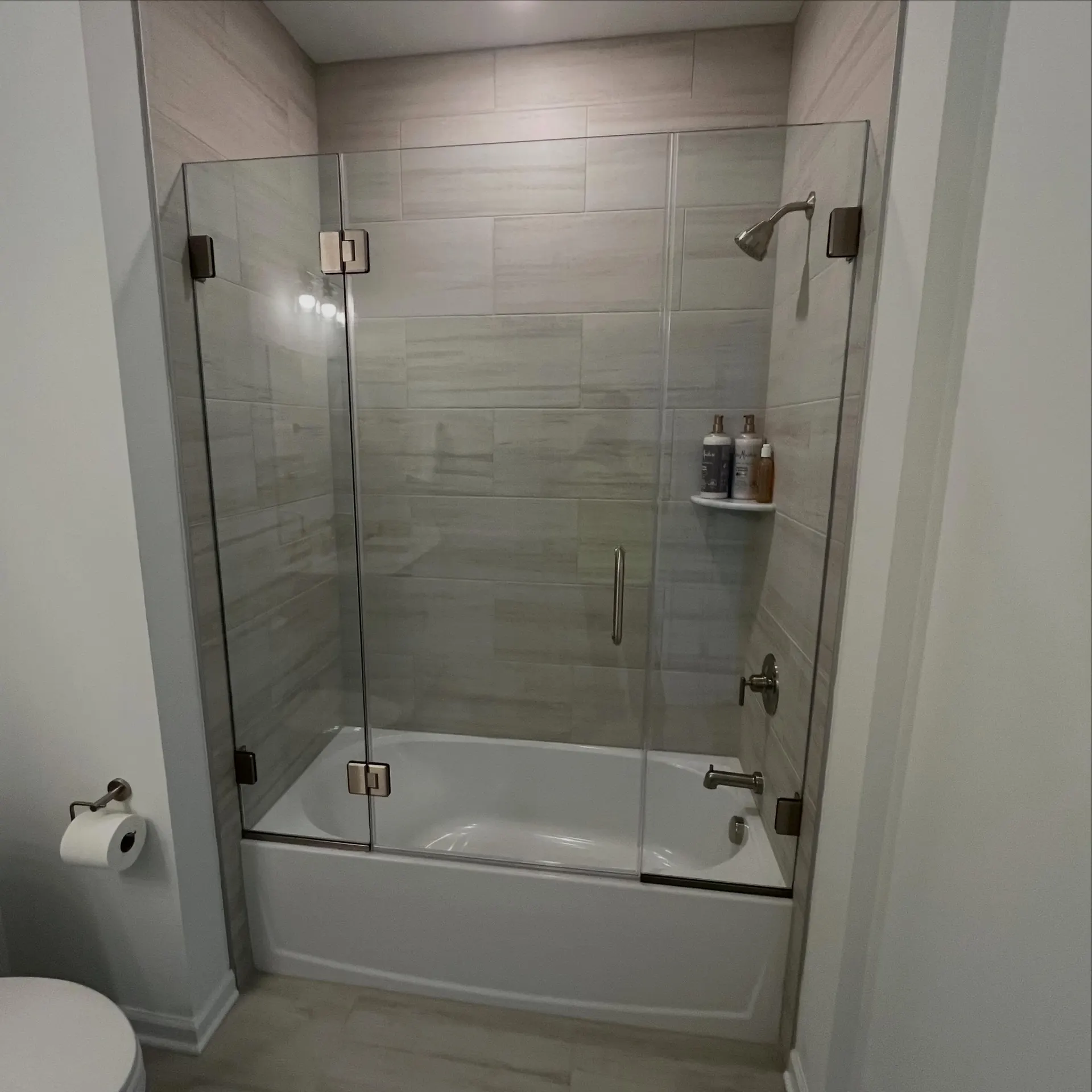 Semi-frameless glass tub enclosure with brushed-nickel hinge hardware, real Mesko Glass installation.