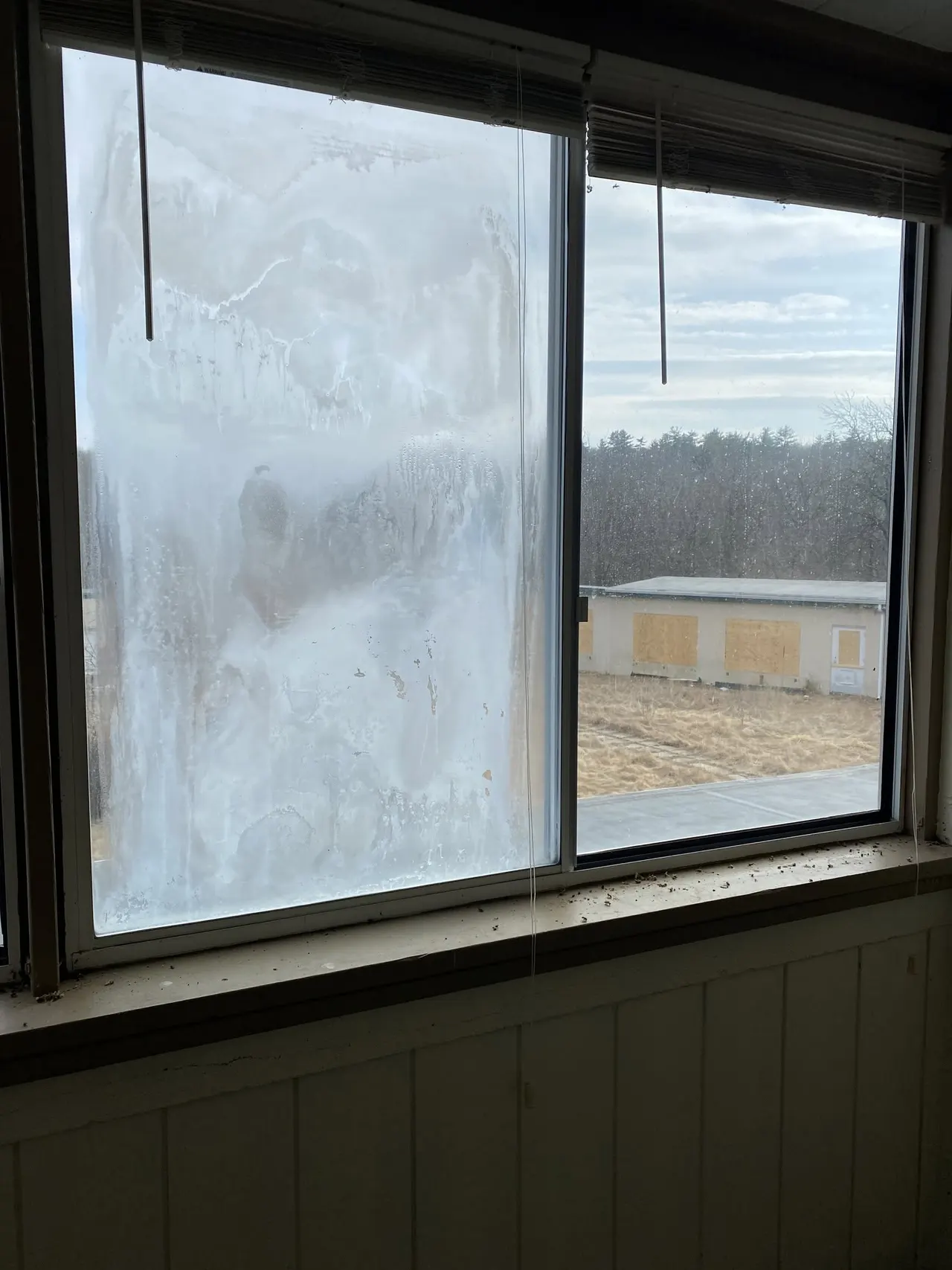 Interior slider window with one sash fogged from a failed insulated glass seal, clear view through the other.