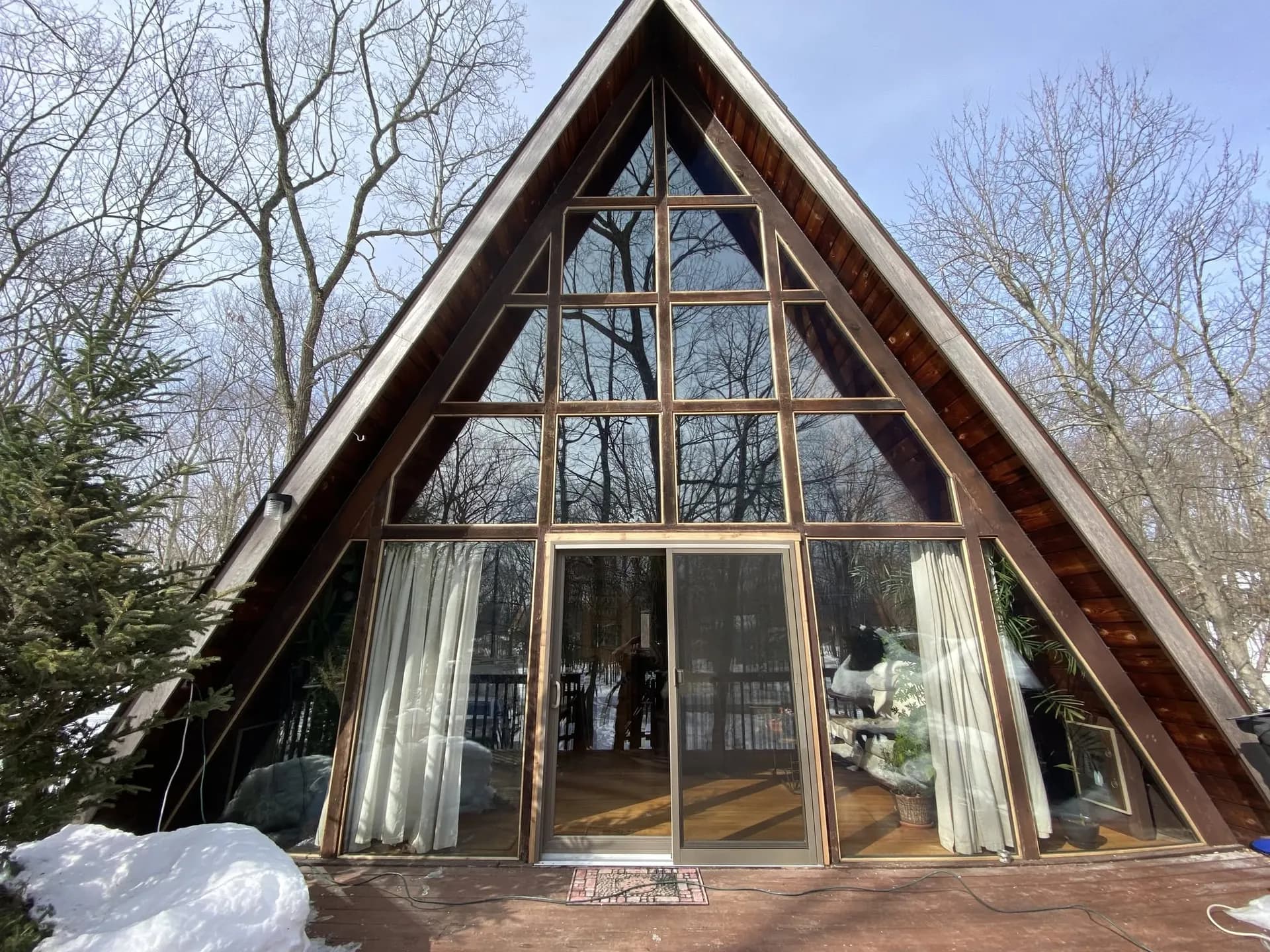 A-frame house with a full glass gable wall and sliding glass doors, snow banked against the deck.