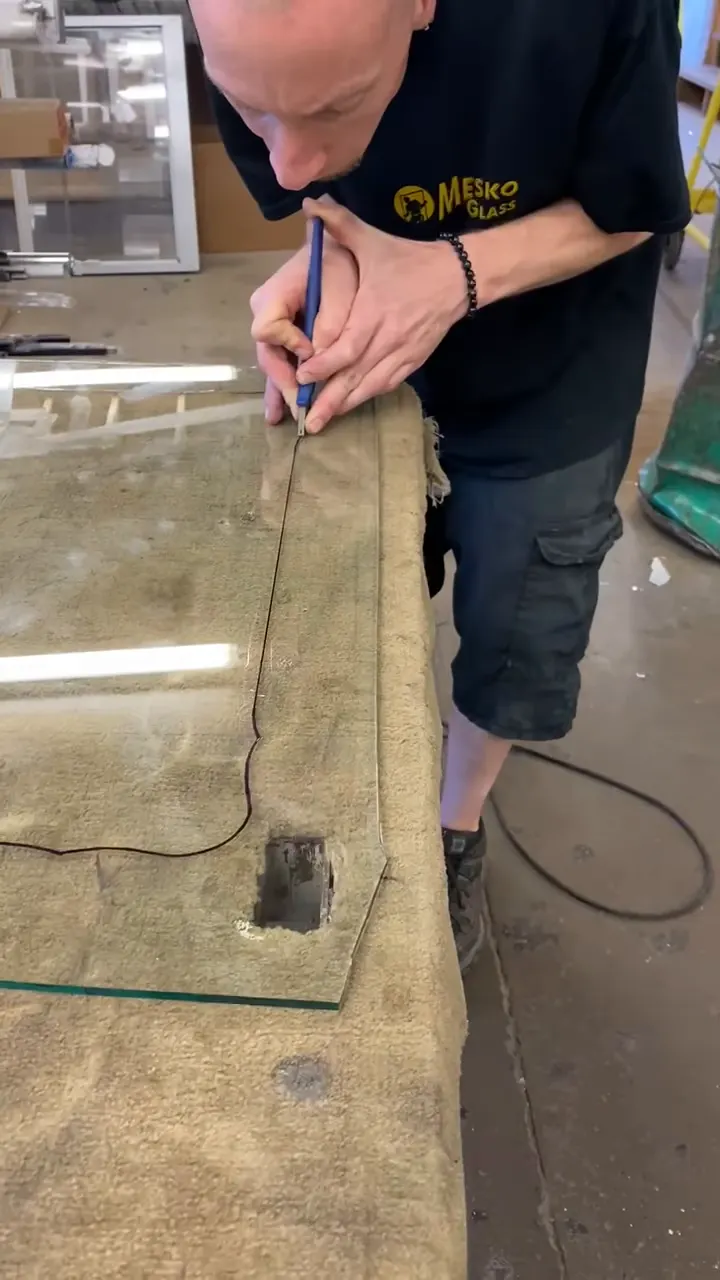 A Mesko glazier scoring and breaking a sheet of glass by hand on the shop bench in East Stroudsburg.