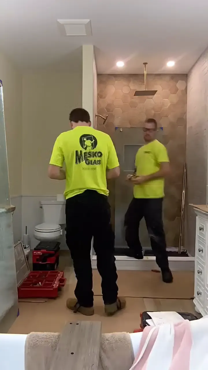 A Mesko installer setting a glass shower panel and fixing the hardware during a real residential install.